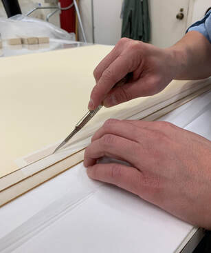 Two hands cutting the back of a flat paper object